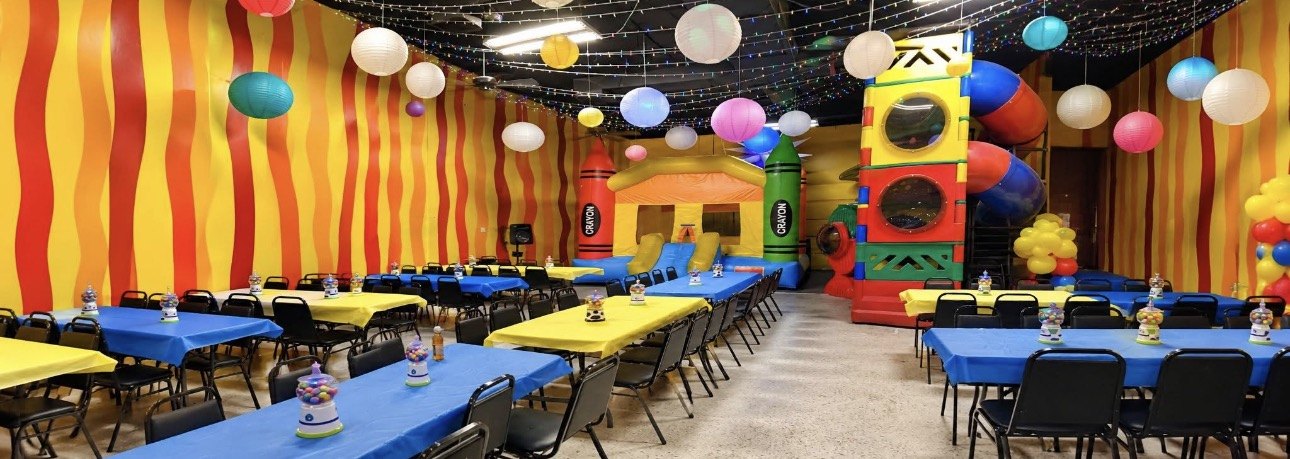 Sunshine Land Party Room 1 with colorful table covers, string lights, paper lanterns, a crayon bounce house and an indoor play structure